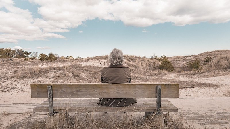 Elderly person sitting on a bench looking at sand dunes