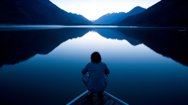 Person sitting quietly on the edge of a dock watching the sunset
