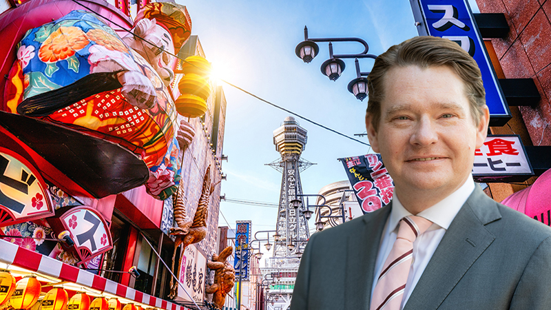 David Mitchinson against a view of Osaka Tower and neon advertisements Shinsekai district