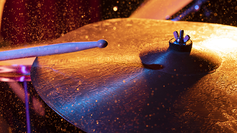Dynamic scene. man playing the drum plate on a colored background, the concept of musical instruments with splashing water on dark background with orange and blue studio lighting