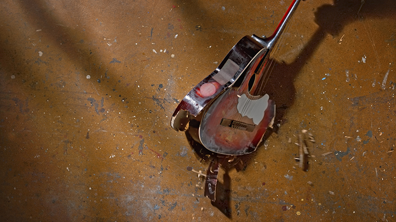 Overhead view of broken guitar falling on floor.