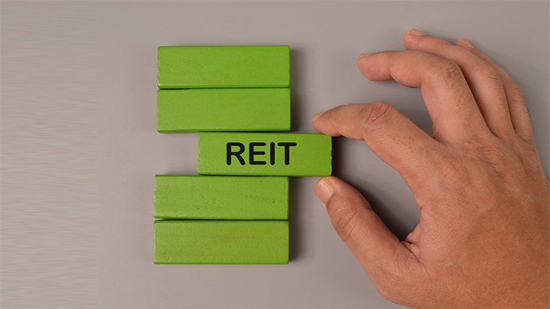 Hand picked wooden block written with REIT stands for Real Estate Investment Trust.