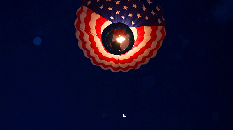 A hot air balloon with an American flag design accends into the night sky, if you look closely you can see a half-moon just below the basket. Albuquerque New Mexico International Balloon Festival. People travel from all over the world to participate in the balloon launch and to sightsee and experience the beautiful hot air balloons in October.