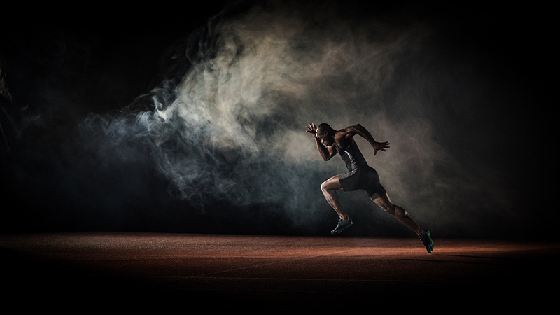 Young male athlete running on race track.