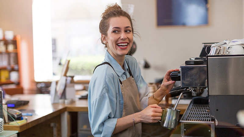 Young barista preparing coffee for customers at her cafe counter