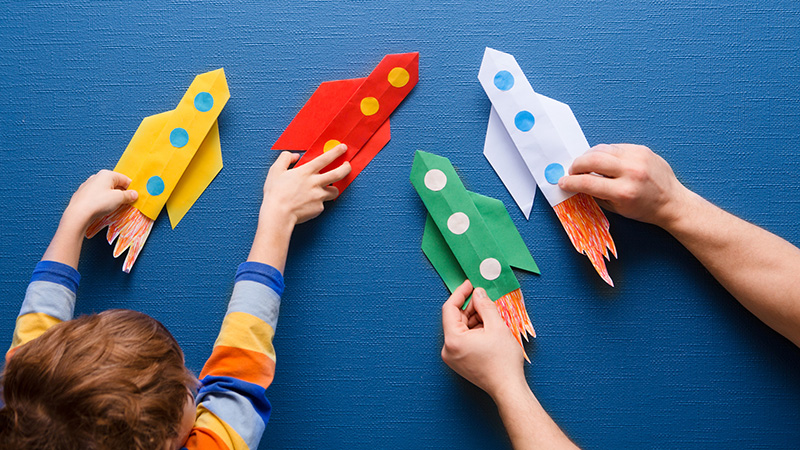 Father and little son are playing with rocket made of paper in the home. Cheerful time together at home. preschool Child in creativity in the home.