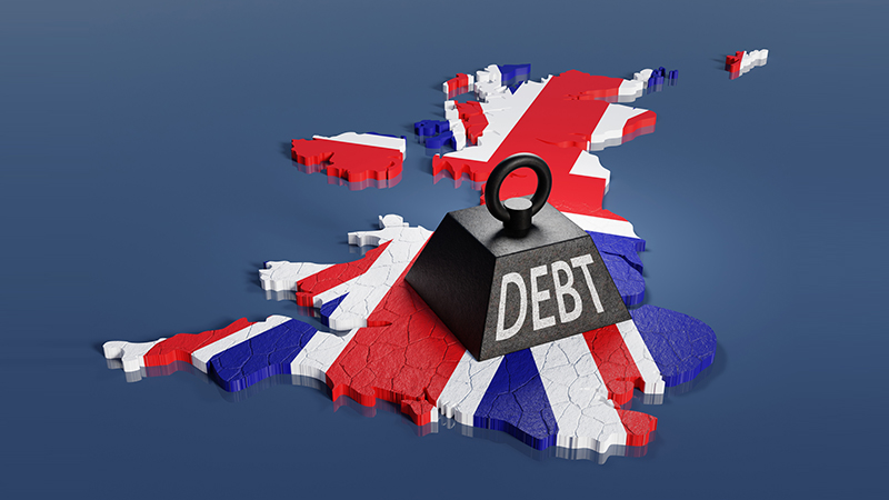 Black one ton weight marked with the word DEBT dropped on the national map of the UK creating cracks. Illustration of the concept of British government debt rises above 100% of GDP