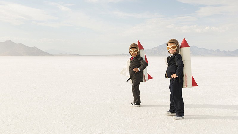 Two young business boys dressed in business suits wearing rockets and aviator goggles are ready to launch their business into the sky. The boys are standing on the Bonneville Salt Flats in Utah, USA.