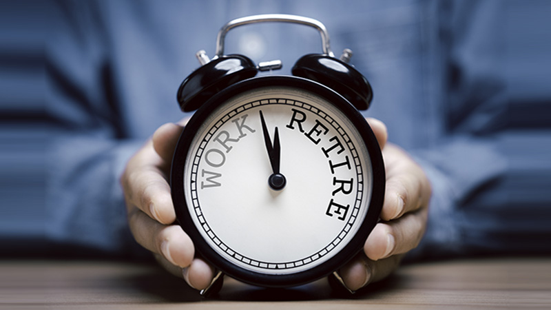 Businessman holding black alarm clock with clockwise countdown from work to retirement.