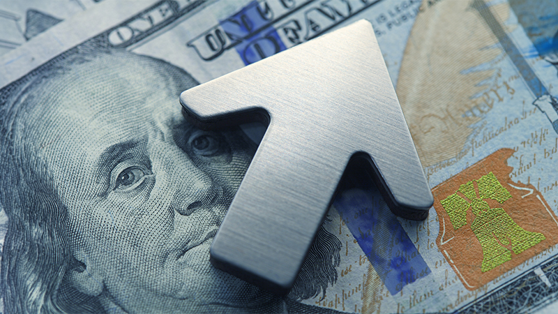 A close up of an upwardly pointing arrow on the face of Benjamin Franklin on the U.S. one hundred dollar bill.