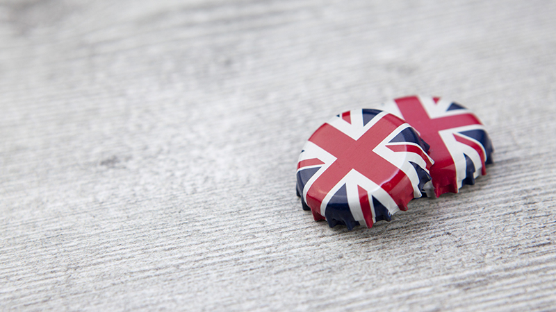 2 Union Jack bottle tops on a rough wooden surface