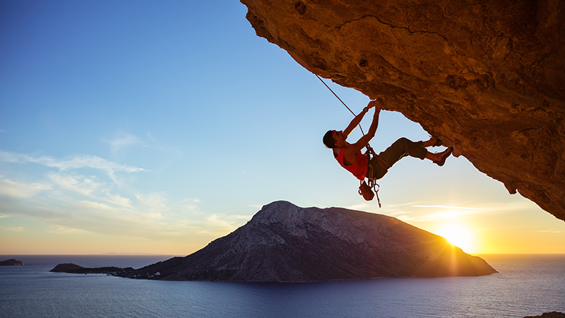 Male climber on overhanging rock at sunset